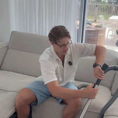 Man using a Magic Brush vacuum cleaner to clean pet hair off a light grey sofa.
